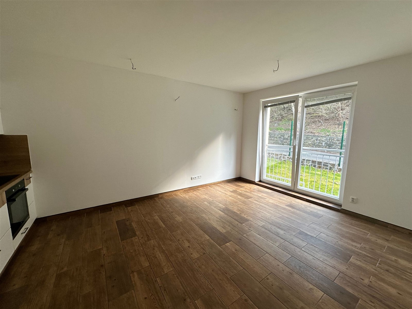 Světlý obývací pokoj s parketovou podlahou, velká okna s výhledem do zahrady, moderní styl a připravený k zařízení.