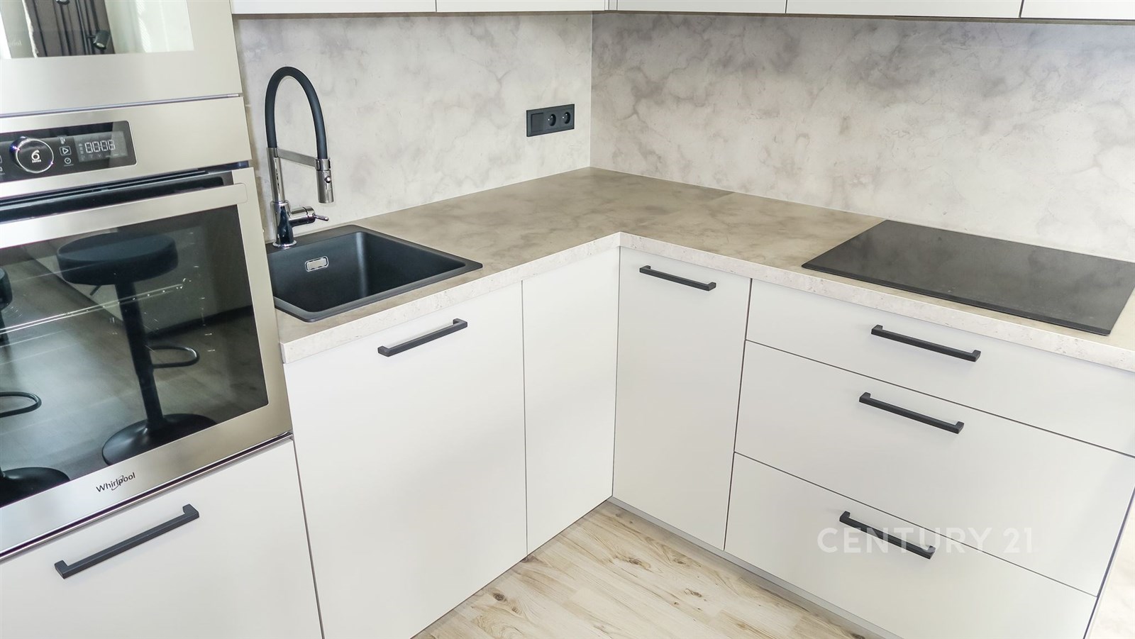 Moderní kuchyň s bílými skříňkami, betonovou pracovní deskou a vestavěnými spotřebiči, světlá dřevěná podlaha, elegantní design.