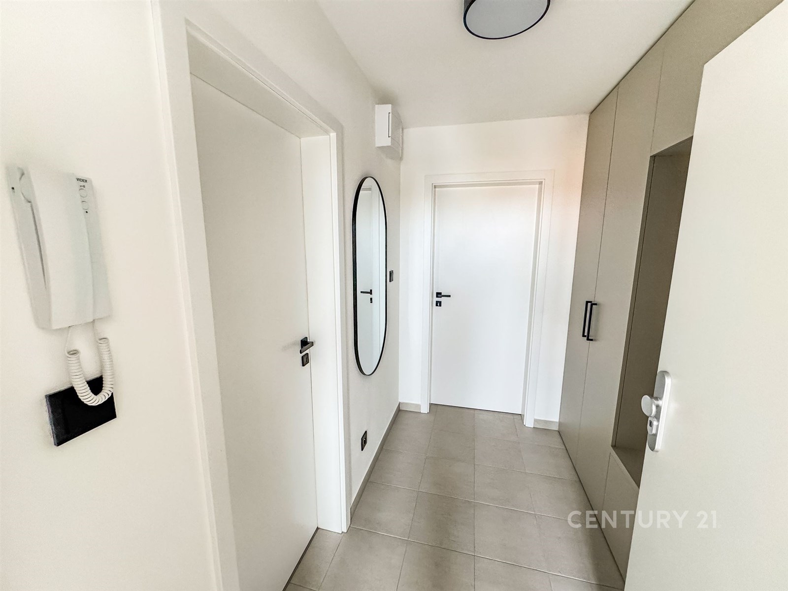 Chodba s dlažbou, vestavěnými skříněmi a moderním designem, světlé stěny a elegantní zrcadlo na stěně