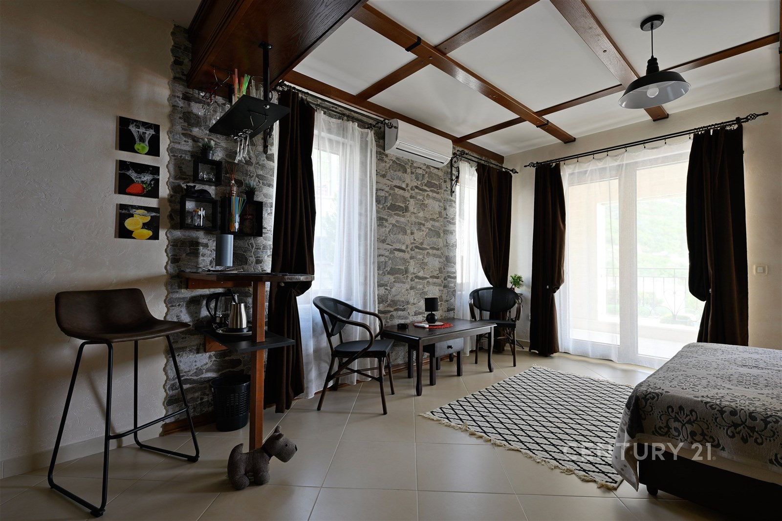 Světlý obývací pokoj s kamennými zdmi, velkými okny a moderním nábytkem, keramická dlažba a elegantní design vytvářejí útulnou atmosféru.
