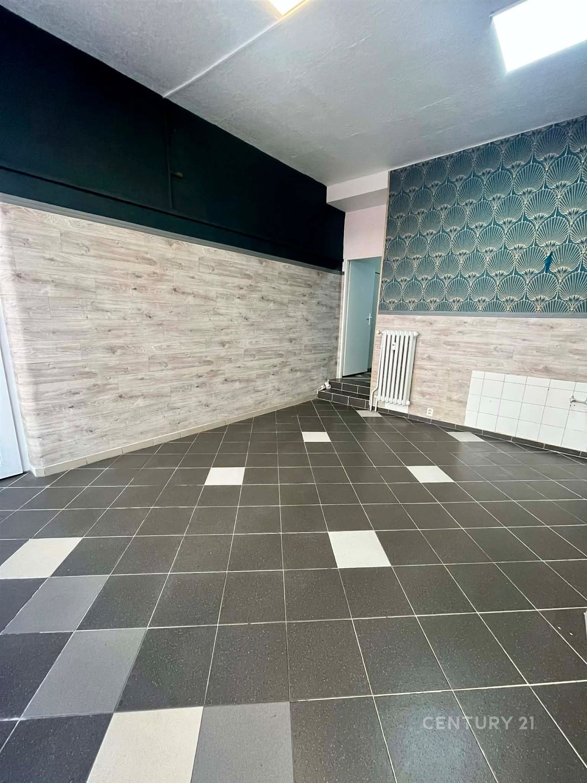 Prostor s dlažbou a dekorativní tapetou, vhodný pro rekonstrukci. Světlé stěny a designový prvek nabízí moderní možnosti využití.