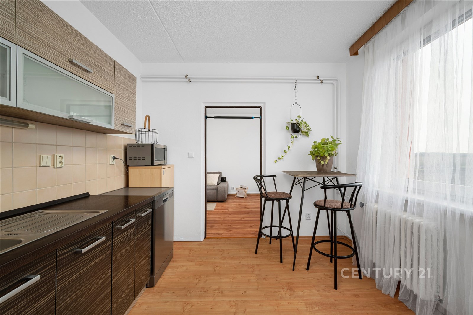 Kuchyňský kout s dřevěnou podlahou a moderními skříňkami, světlý prostor s velkými okny a jídelním stolem, ideální pro pohodlné bydlení.