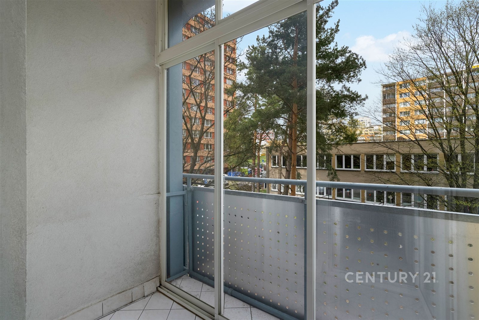 Balkon s dlažbou a skleněným zábradlím nabízí výhled na město, ideální pro moderní bydlení a relaxaci v klidném prostředí.