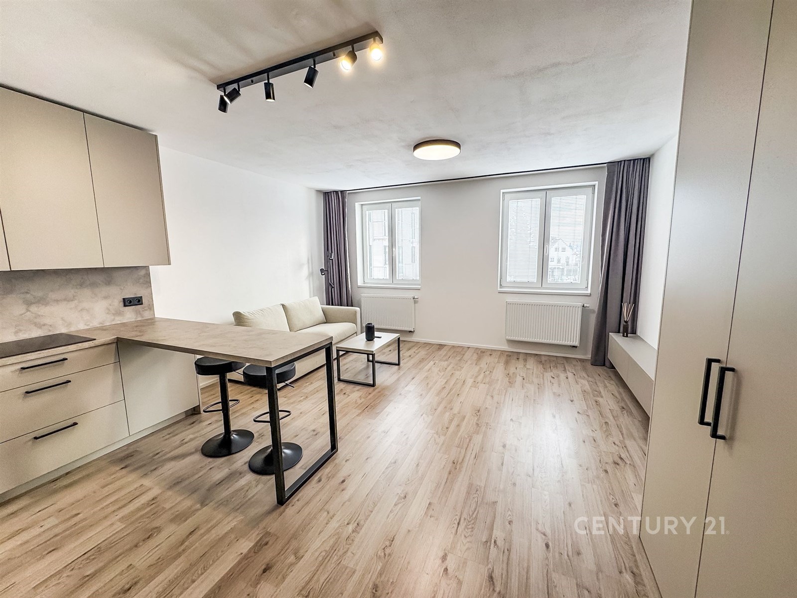 Světlý obývací pokoj s moderní kuchyní, parketová podlaha, velká okna a světlé stěny vytvářejí pocit prostornosti, zrekonstruovaný styl.