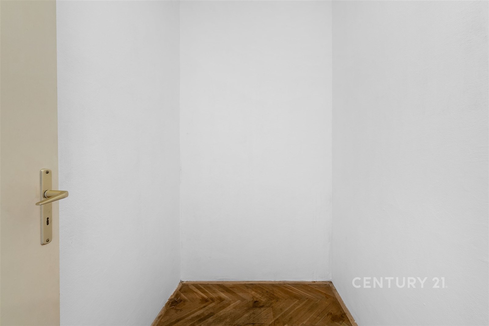 Malý úložný prostor s dřevěnou parketovou podlahou a bílými stěnami, ideální pro vestavěné skříně nebo skladování v moderním bytě.