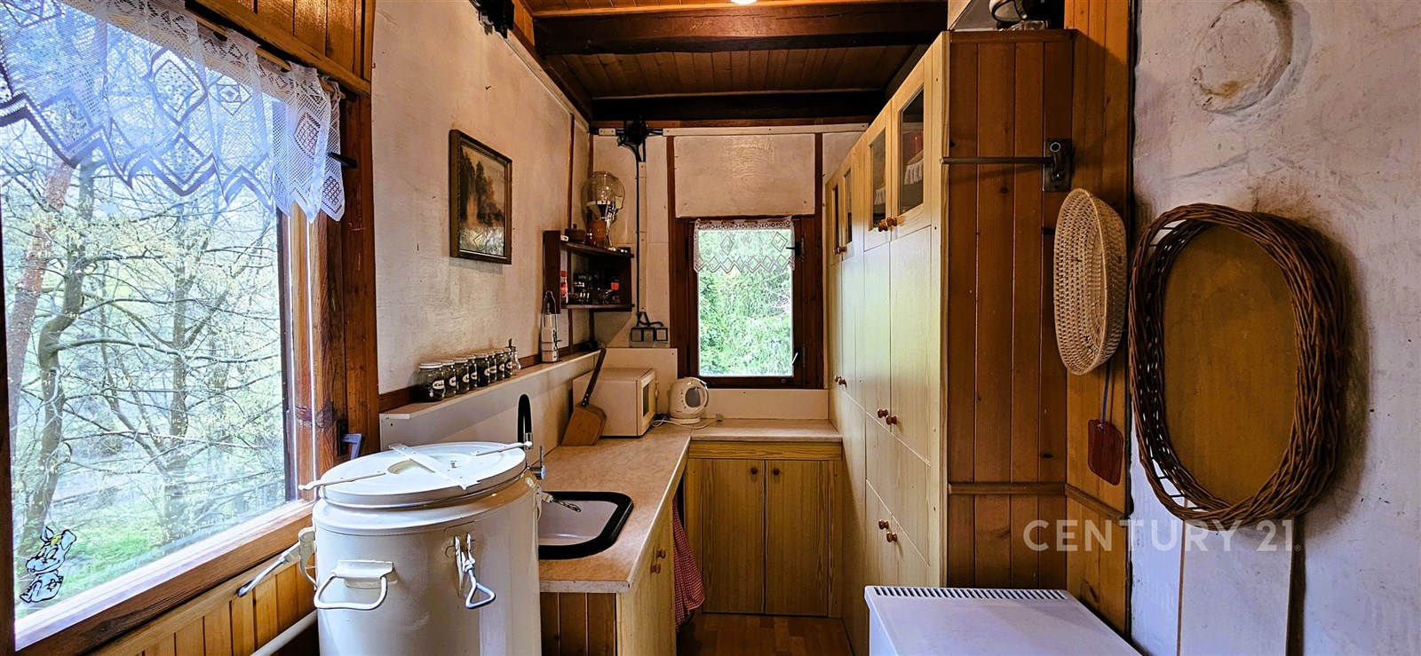 Kompaktní kuchyň, dřevěná povrchová úprava, vestavěné skříně, výhled do přírody, rustikální styl, funkční uspořádání.