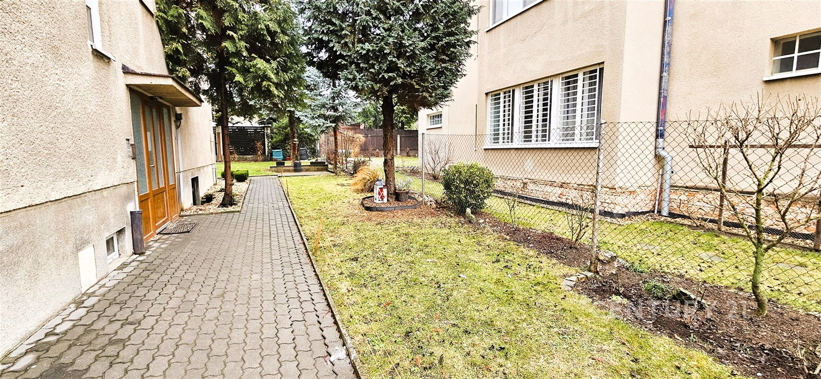 Úzká přístupová cesta s dlažbou, oplocená zahrada,