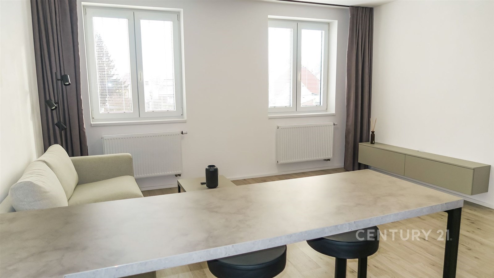 Moderní obývací pokoj s parketovou podlahou, velká okna zajišťující světlo, elegantní barový pult v minimalistickém stylu.