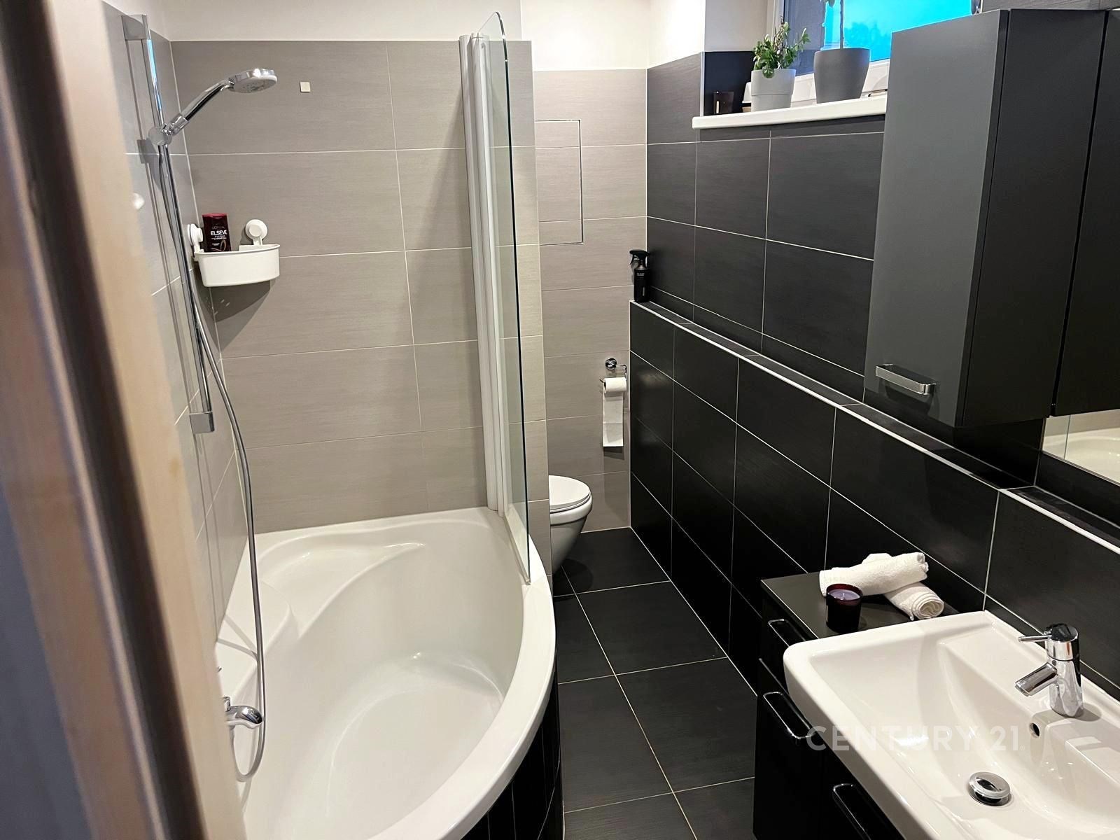 Moderní koupelna s dlažbou, rohovou vanou a tmavým