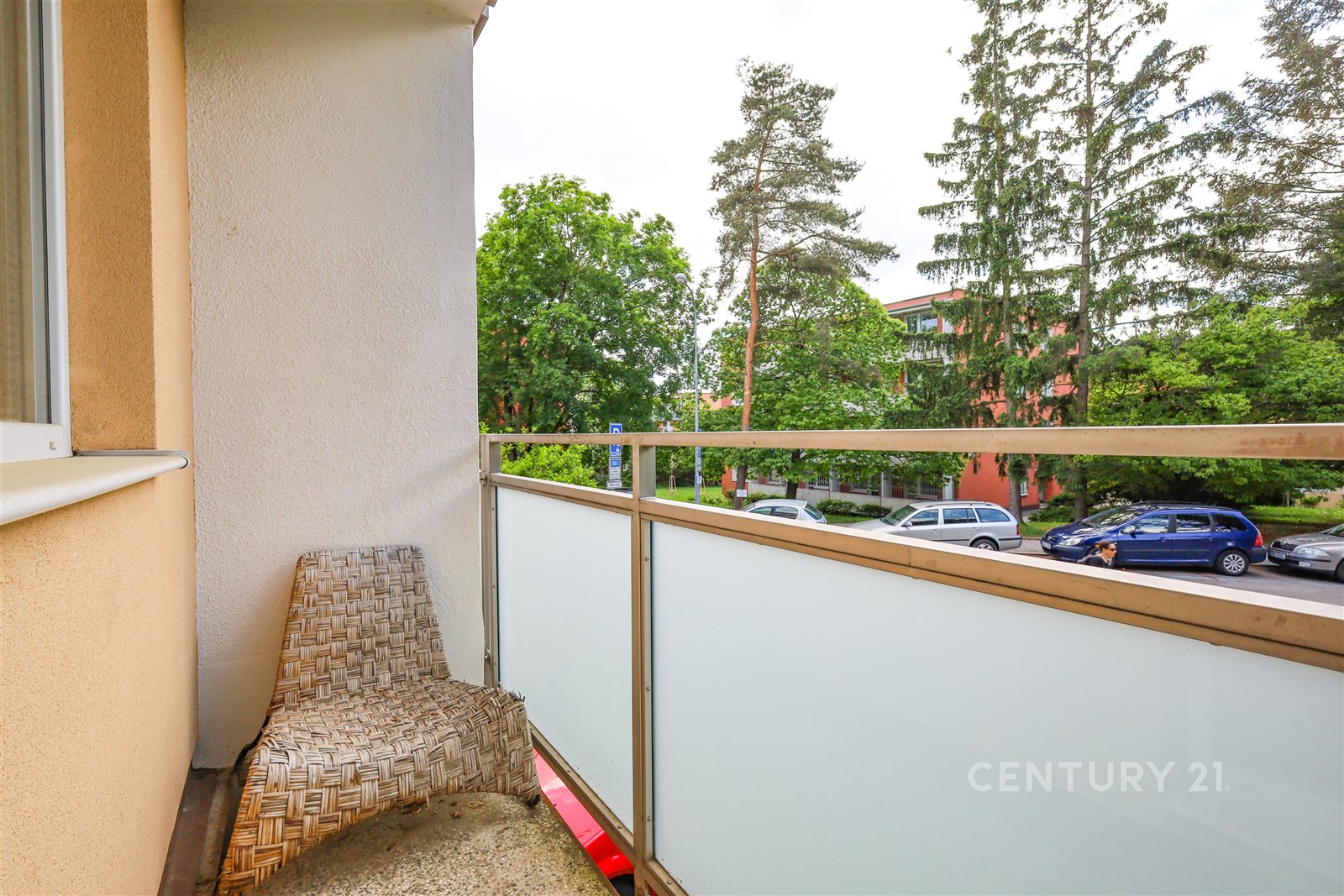 Balkon s výhledem na ulici, vybavený moderním skleněným zábradlím a přírodní dlažbou, nabízí klidné venkovní posezení v zeleni.