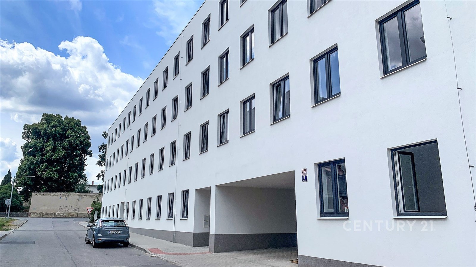 Exteriér bytového domu s moderní fasádou, plastová okna a čisté linie, dobrý stav budovy.