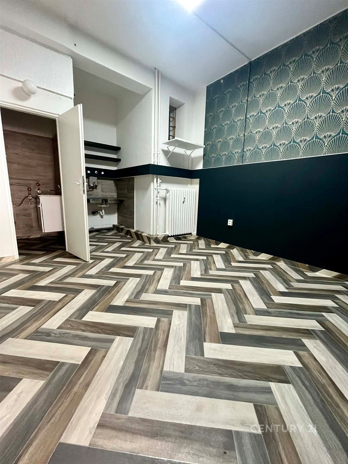 Moderní kuchyň s parketovou podlahou ve vzoru, stylové tapety a klasické radiátory, ideální pro rekonstrukci.