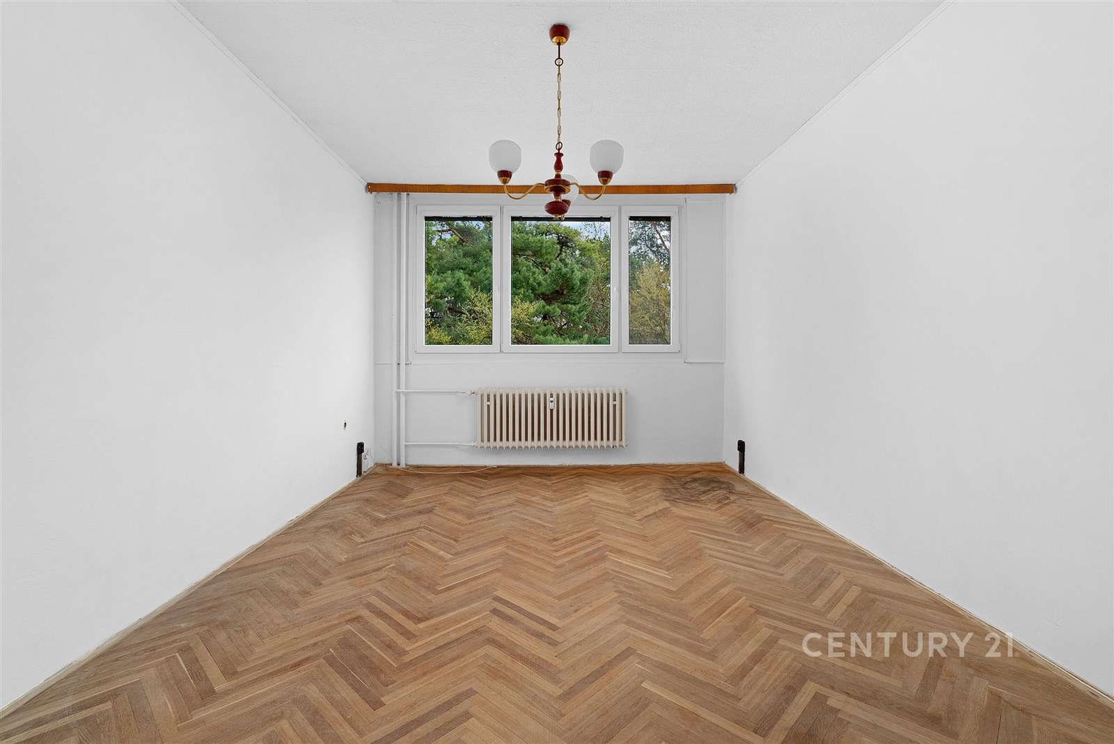 Pokoj s parketovou podlahou, velkými okny a bílými stěnami, světlý a připravený k rekonstrukci.