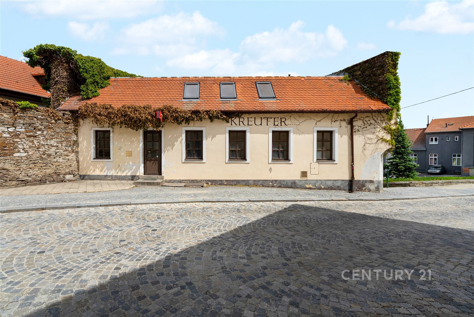Starší komerční budova s červenou střechou, kamennou fasádou a dlažbou na příjezdové cestě, vhodná pro podnikání v historické části města.