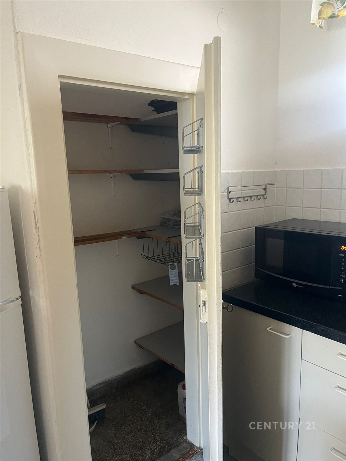 Praktická spíž s policemi, dlažbou a bílými stěnami, přiléhající k moderní kuchyni s mikrovlnnou troubou a úložným prostorem.