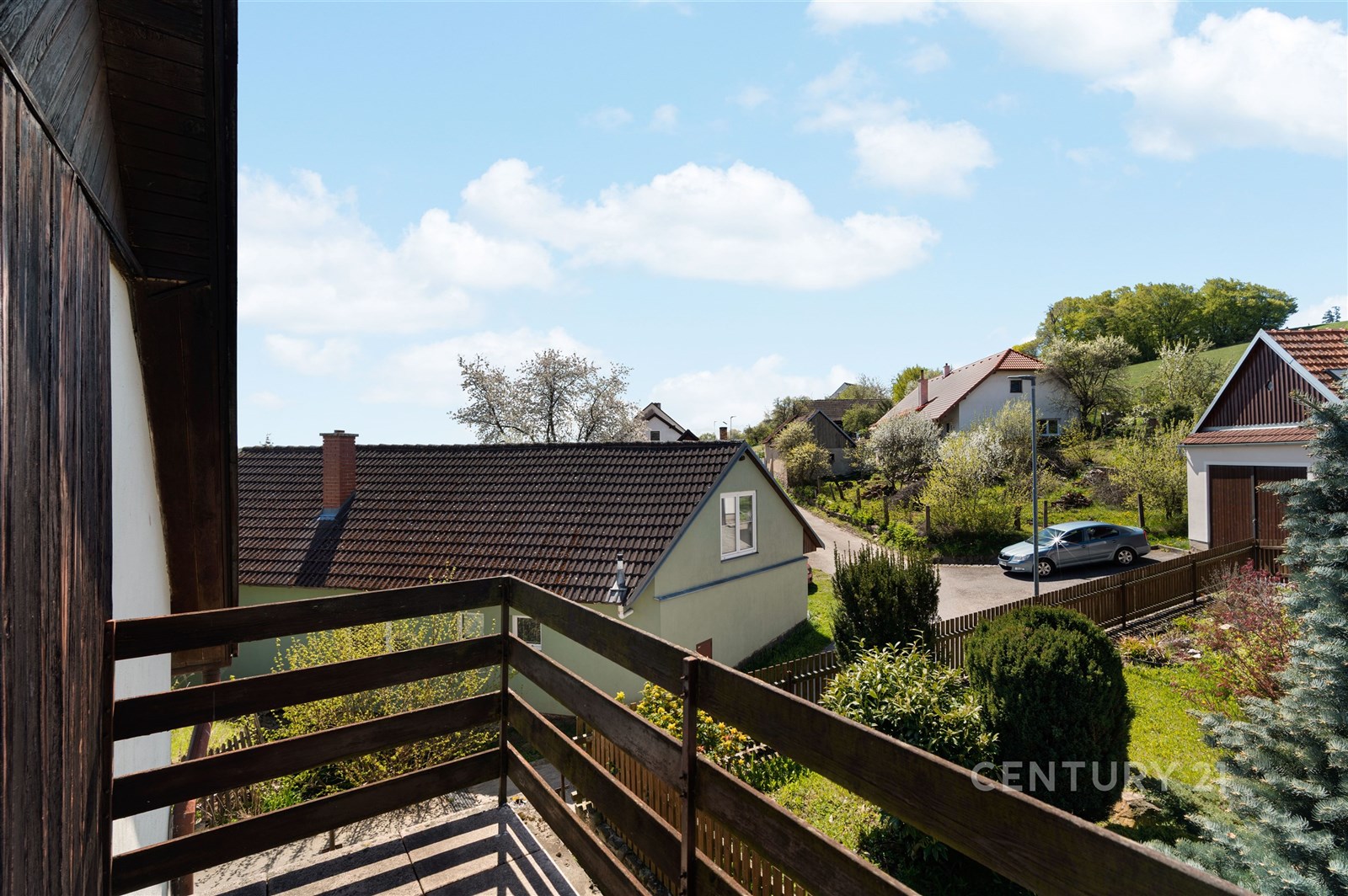 Balkon s dřevěným zábradlím a výhledem na poklidnou vesnickou krajinu, ideální pro relaxaci a klidné bydlení
