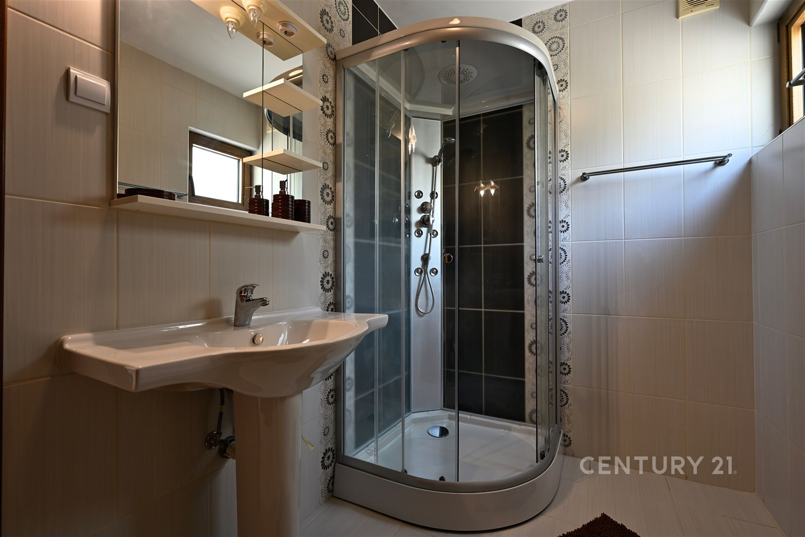 Moderní koupelna s elegantní sprchovým koutem, keramickou dlažbou a velkým zrcadlem. Světlé stěny a kvalitní vybavení zajišťují komfort.
