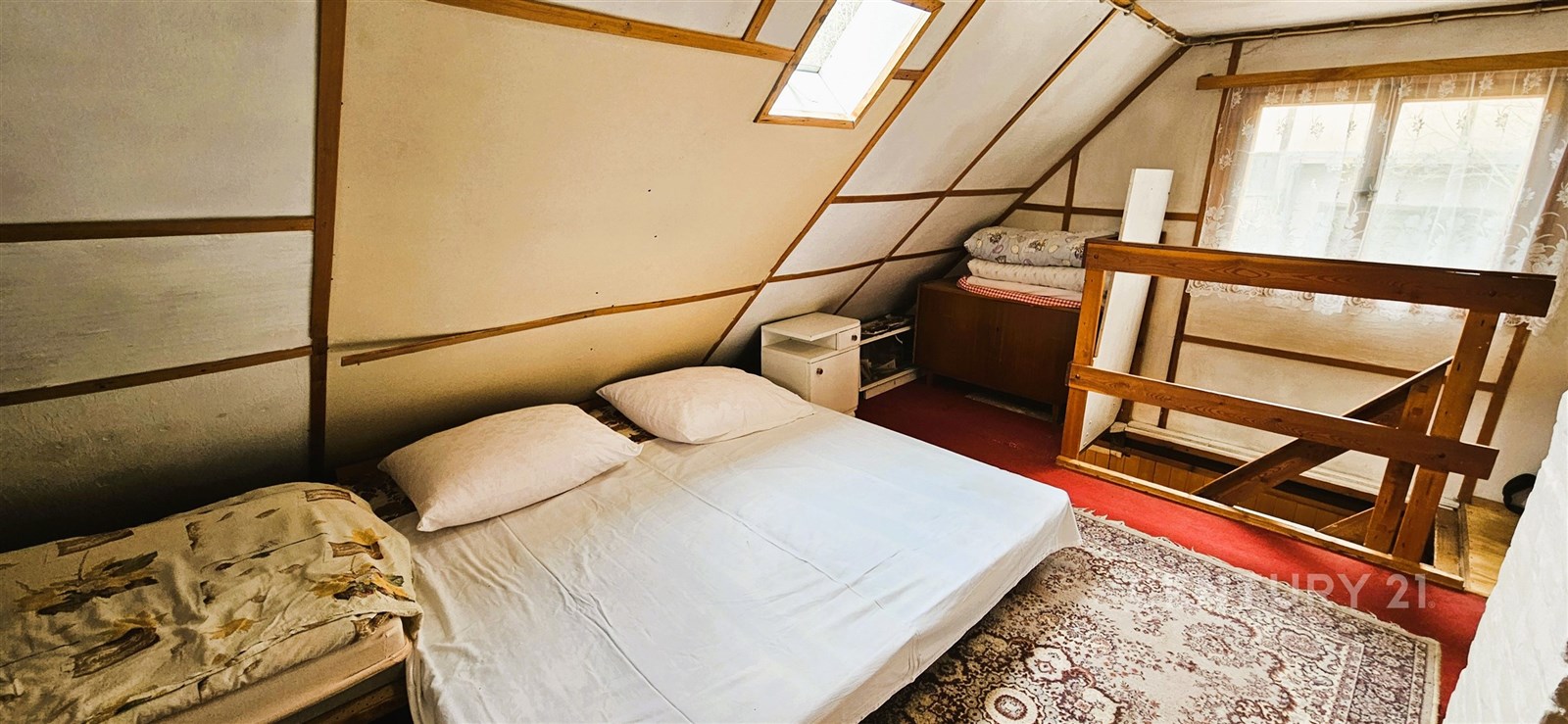 Podkrovní ložnice se šikmým stropem, světlá, s dřevěnými prvky, koberce na podlaze, okno pro denní světlo, venkovský styl.