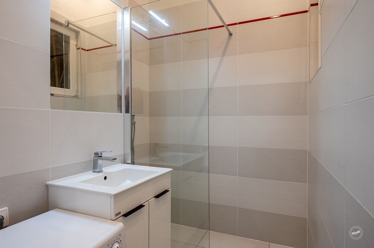 Koupelna s moderním designem, sprchovým koutem a světlými dlaždicemi, nabízí elegantní čisté linie a praktické úložné prostory.