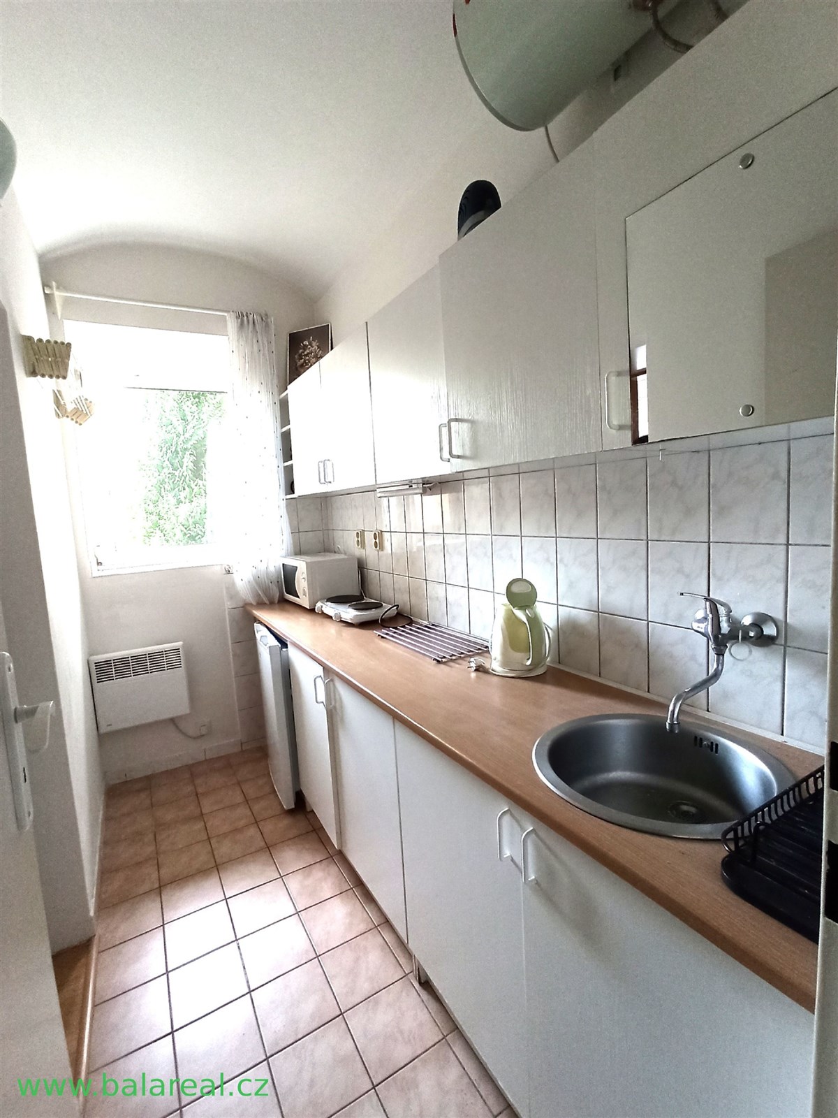 Úzká kuchyň s dlažbou, bílými skříňkami a dřevěnou