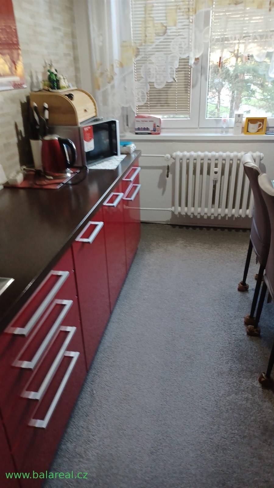 Kuchyň s červenými skříněmi a moderními úchyty, laminátový povrch, světlý prostor s velkým oknem, útulný styl