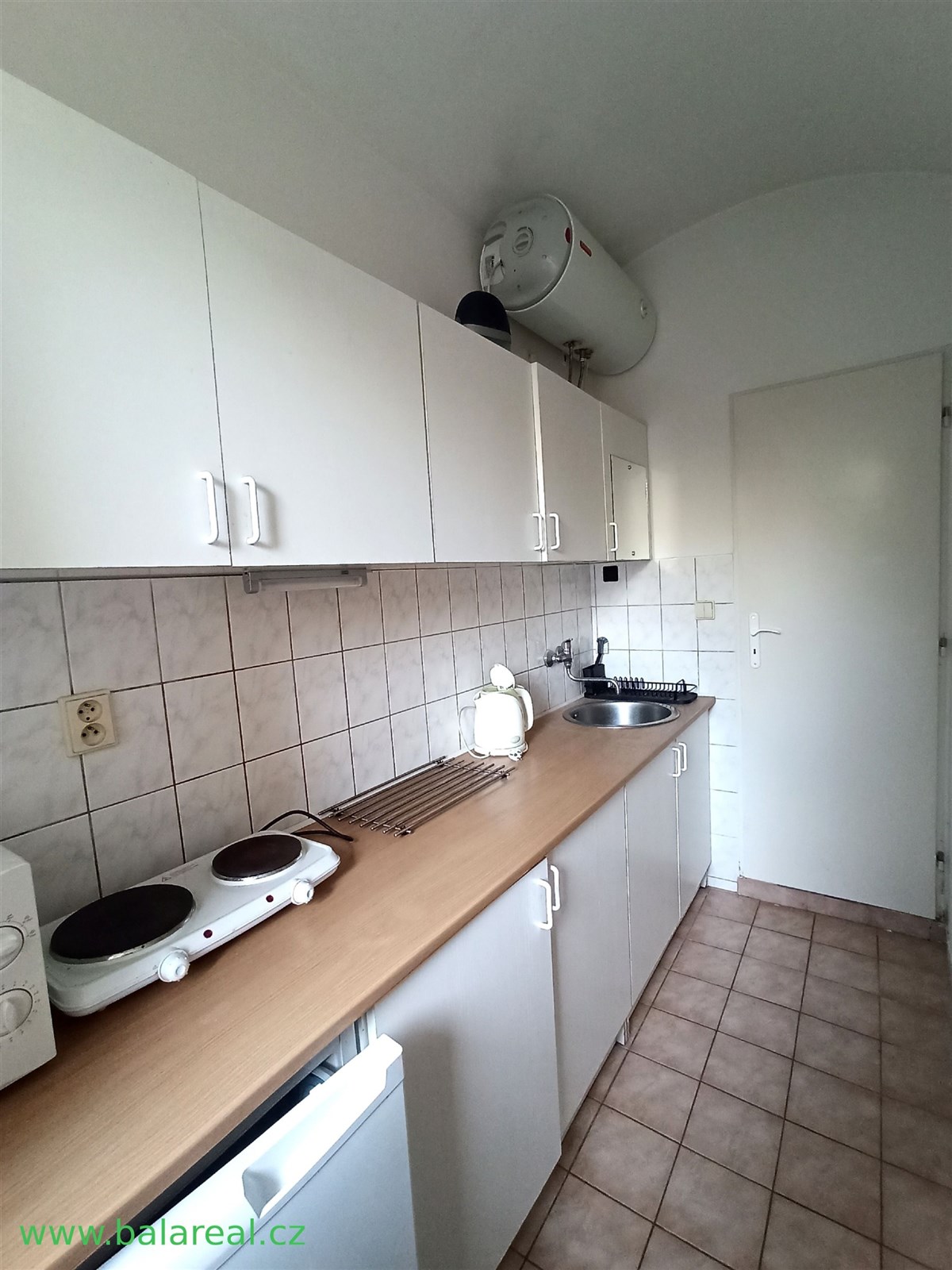 Úzká kuchyň s dlažbou a světlými skříňkami, vybave