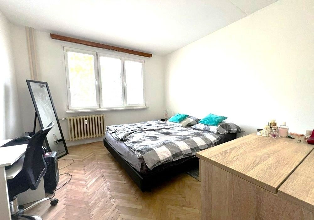 Světlá ložnice s parketovou podlahou, velkými okny a moderním nábytkem, nabízí komfortní prostor pro odpočinek a relaxaci.