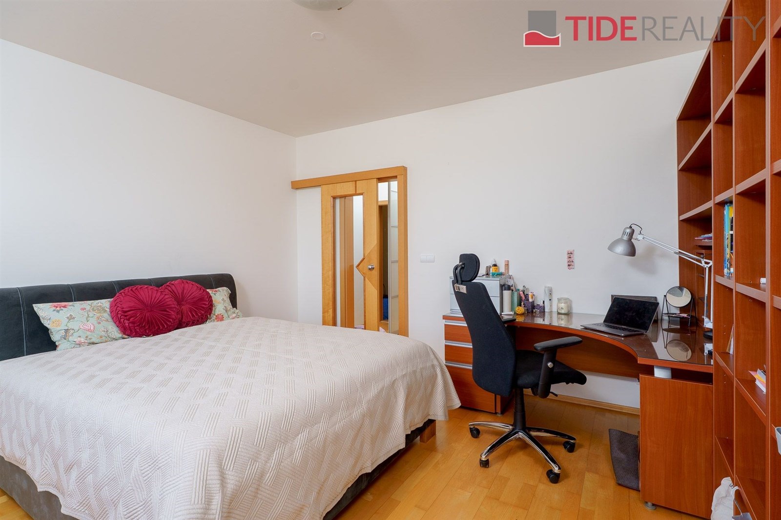 Ložnice s parketovou podlahou, moderní nábytek a vestavěný pracovní koutek, velká knihovna.