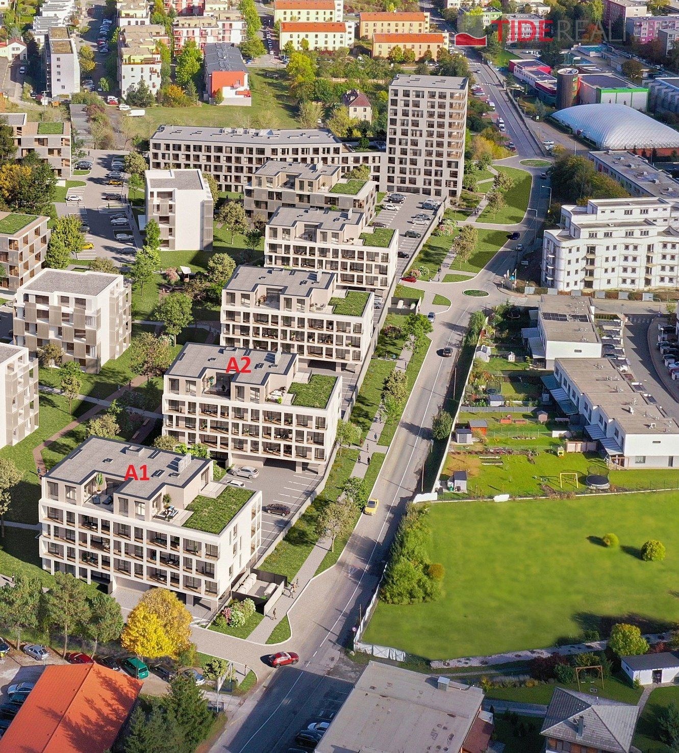 Satelitní pohled na moderní bytový komplex s travnatými střechami, širokými terasami a parkovacími místy, situovaný v klidném městském prostředí.