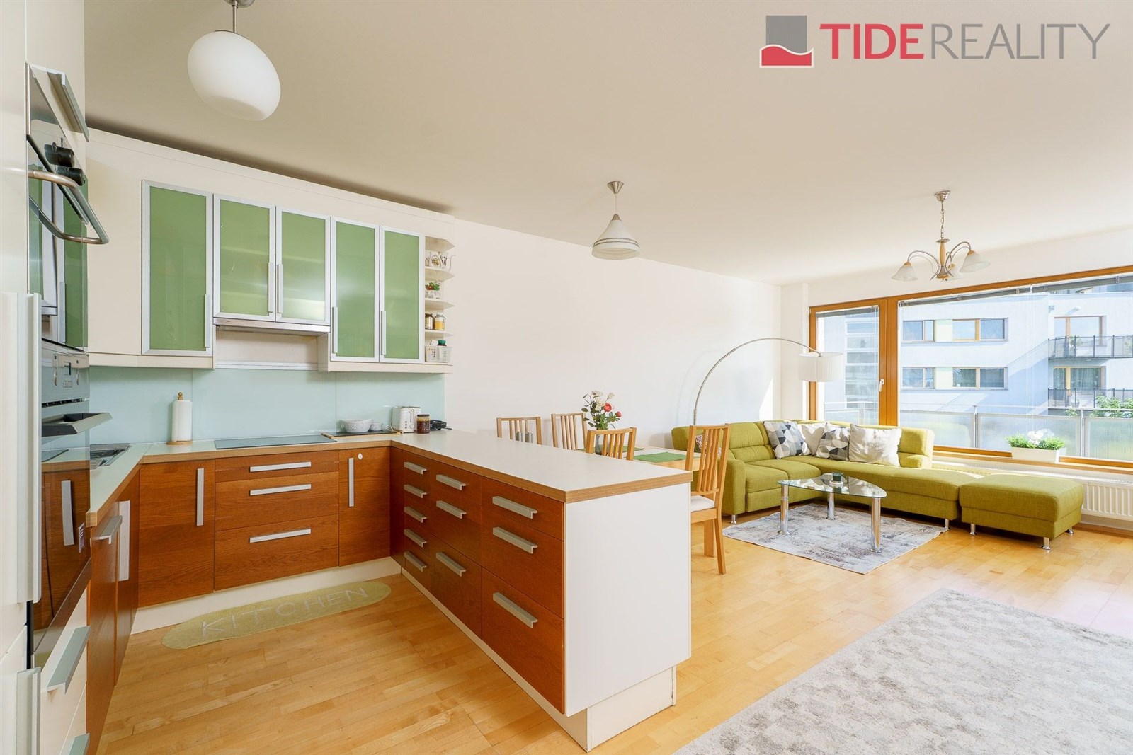 Moderní kuchyň s parketovou podlahou, vestavěnými skříněmi a velkými okny propojená s obývacím pokojem v světlém stylu.