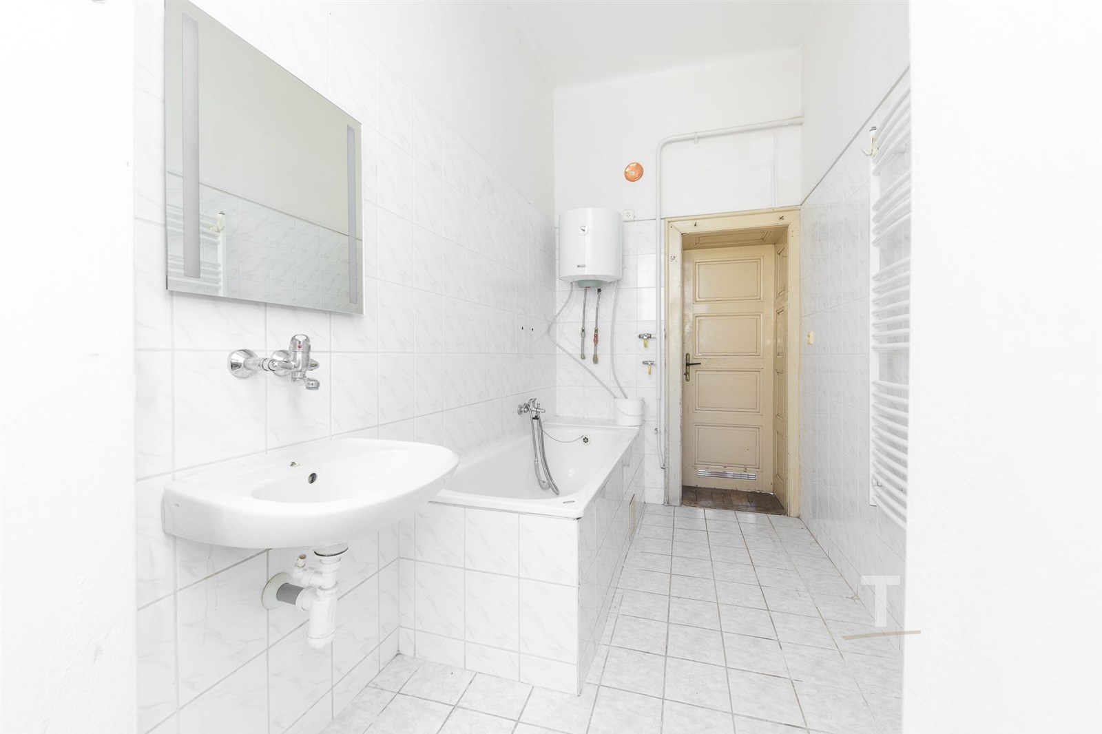 Prostorná koupelna s bílými dlaždicemi, vanou a za