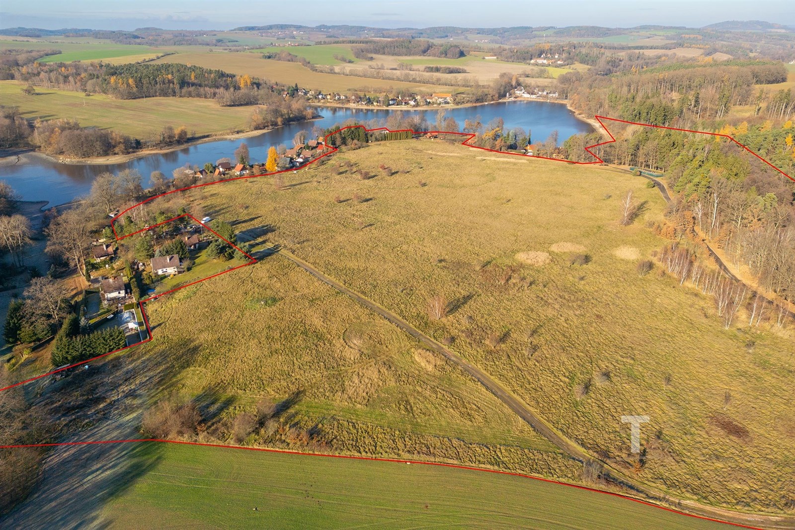 Letecký pohled na rozsáhlý pozemek s výhledem na jezero, obklopený zelení a přírodou, ideální pro výstavbu rodinných domů nebo rekreačních objektů.