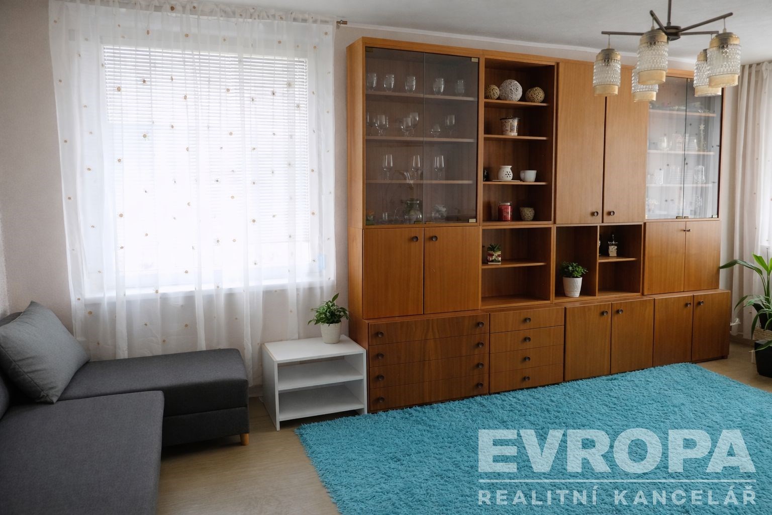 Světlý obývací pokoj s parketovou podlahou a velkou obývací stěnou z dřeva, nabízí útulný prostor s moderním nábytkem a velkými okny.