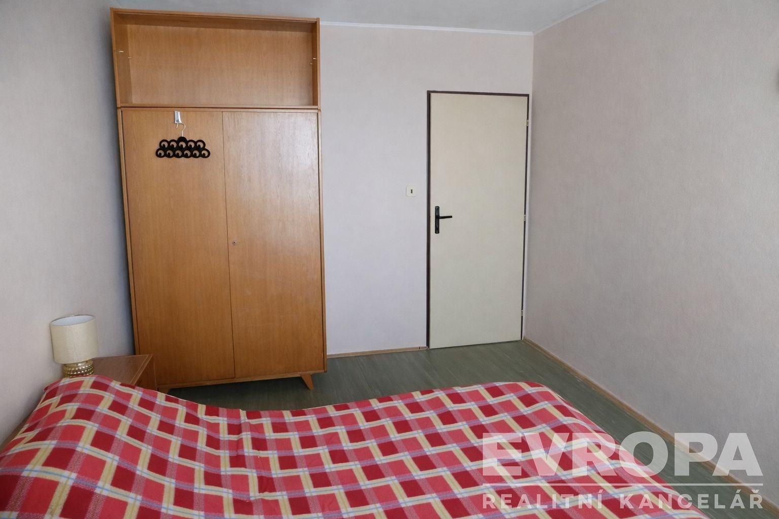 Ložnice s parketovou podlahou, jednoduchou dřevěnou skříní a světlými stěnami, moderní a čistý design interiéru.