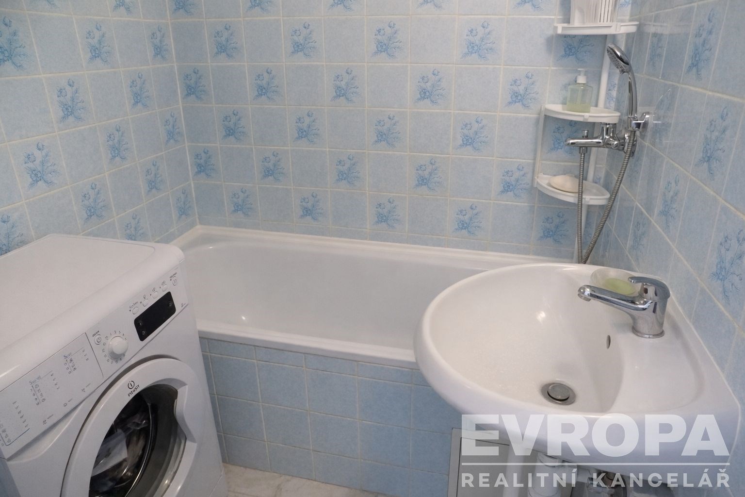 Kompaktní koupelna s vanou, světlými kachlovými obklady a praktickou vestavěnou pračkou, nabízí funkční využití prostoru