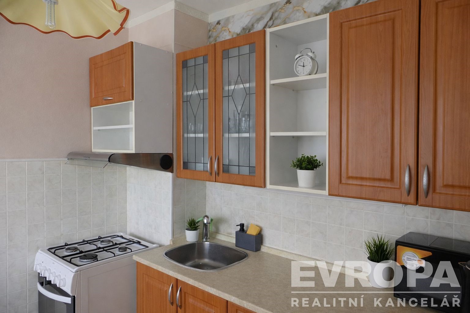 Kuchyň v klasickém stylu s dřevěnými skříňkami, světlou pracovní deskou a moderními spotřebiči, keramická dlažba na zdi