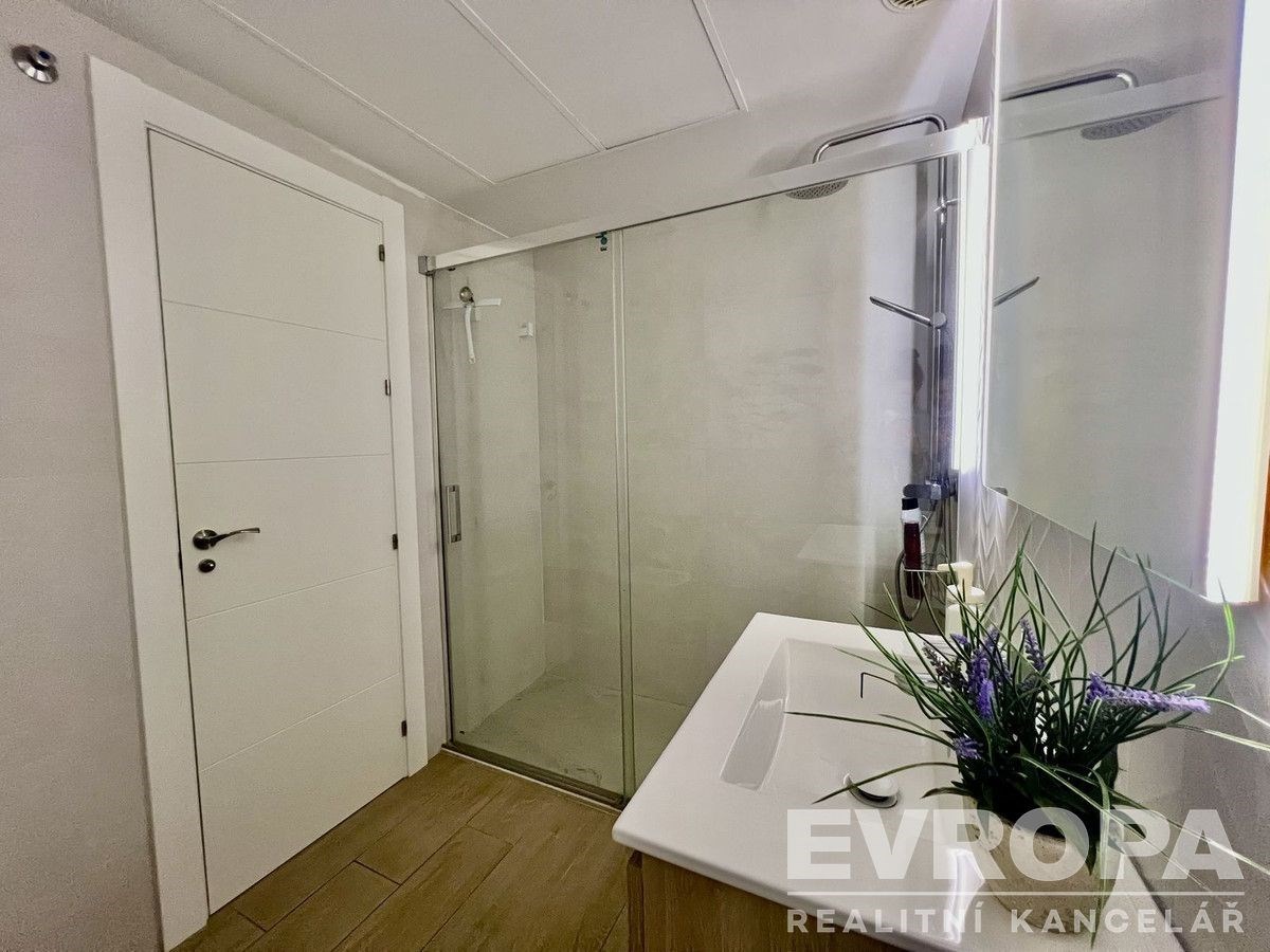 Moderní koupelna s velkým sprchovým koutem, světlá dlažba a elegantní dřevěný nábytek vytvářejí stylový a čistý vzhled.