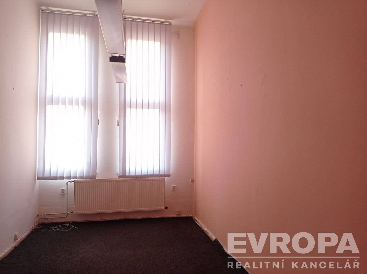 Malá kancelář s kobercovou podlahou, velkými okny a vertikálními žaluziemi, v udržovaném stavu