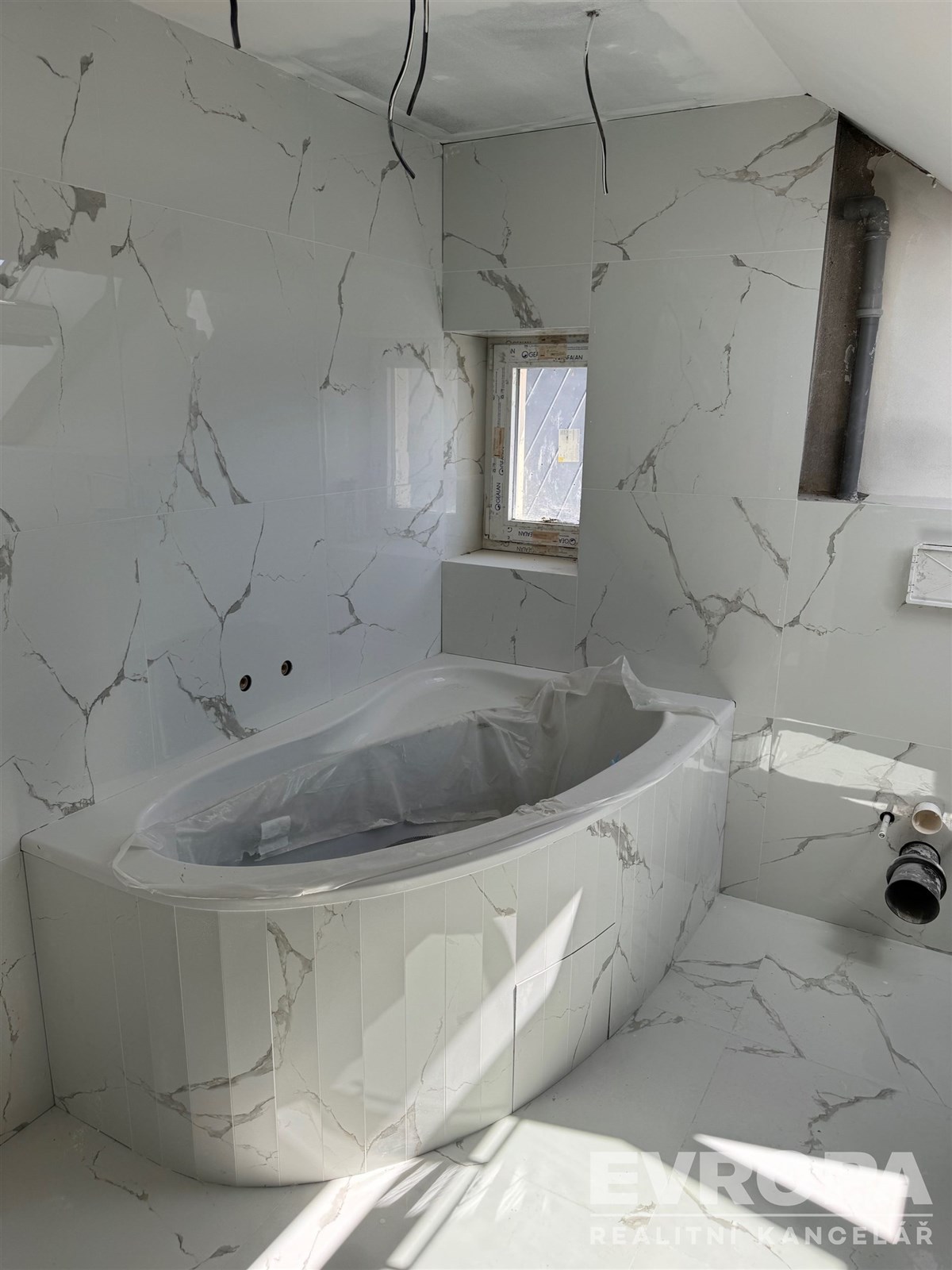 Luxusní koupelna s mramorovou dlažbou, moderní vanou a světlými obklady, ideální pro relaxaci v elegantním prostředí.