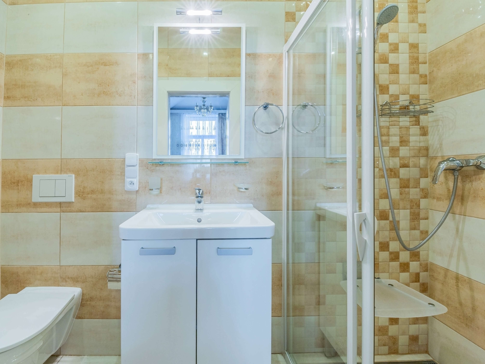 Koupelna se sprchovým koutem, umyvadlovou skříňkou a WC. Moderní obklady v béžových tónech, dobré osvětlení.