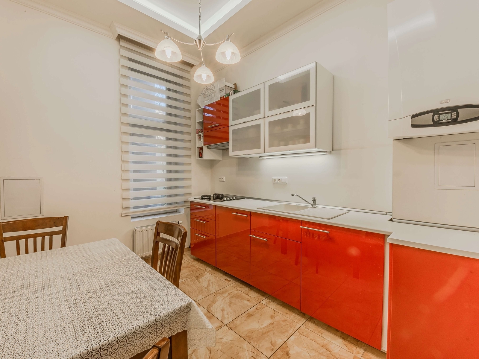 Moderní kuchyň s červenou linkou a skříňkami s mléčným sklem, jídelní kout. Plynový kotel a varná deska.