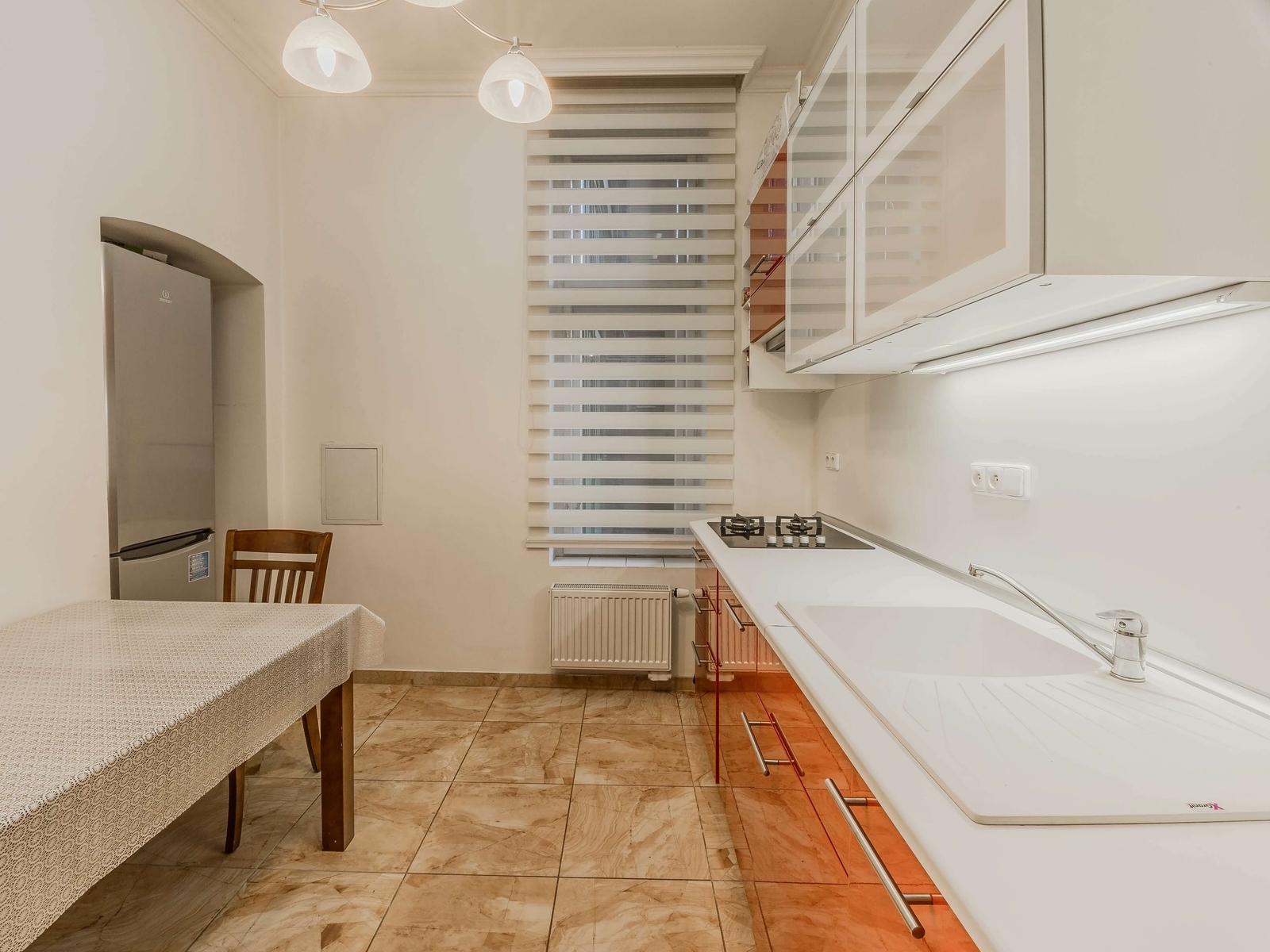 Kuchyně s červenou linkou, jídelním stolem a lednicí v nice. Vysoký strop, den-noc rolety a plynová varná deska.