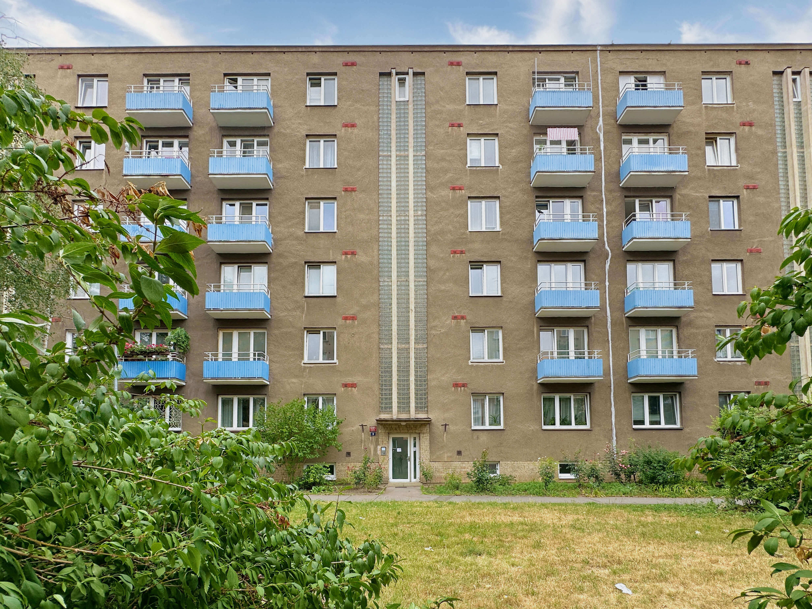 Čelní pohled na dům s modrými balkony a zatravněno