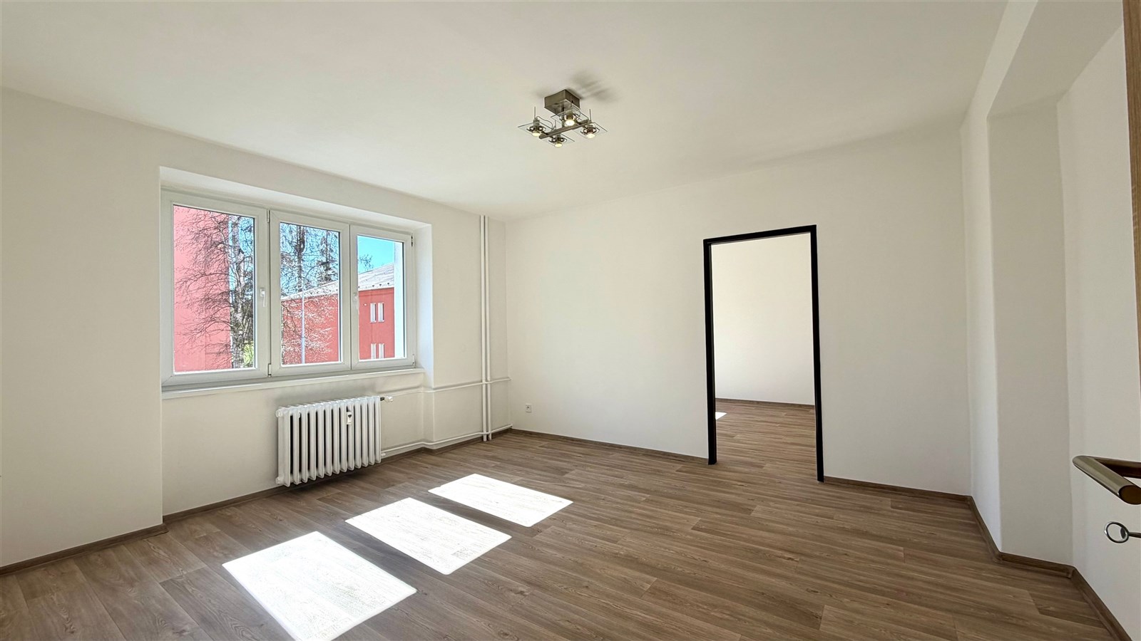 Světlý obývací pokoj, parketová podlaha, velká okna, moderní styl, nově rekonstruovaný, výhled na okolní budovy.