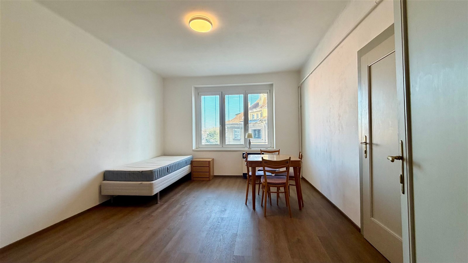 Světlá ložnice s parketovou podlahou, velkými okny a moderním nábytkem, ideální pro minimalistický styl bydlení.