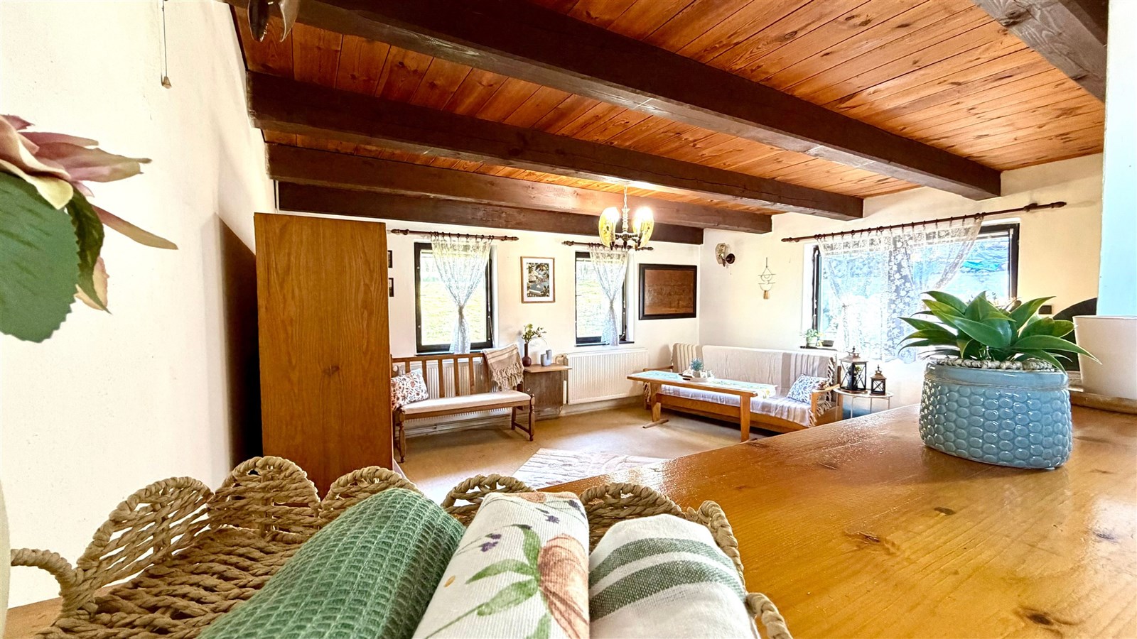 Rustikální obývací pokoj s dřevěným stropem, parketovou podlahou a velkými okny, které zajišťují světlou atmosféru a zároveň nabízejí krásný výhled