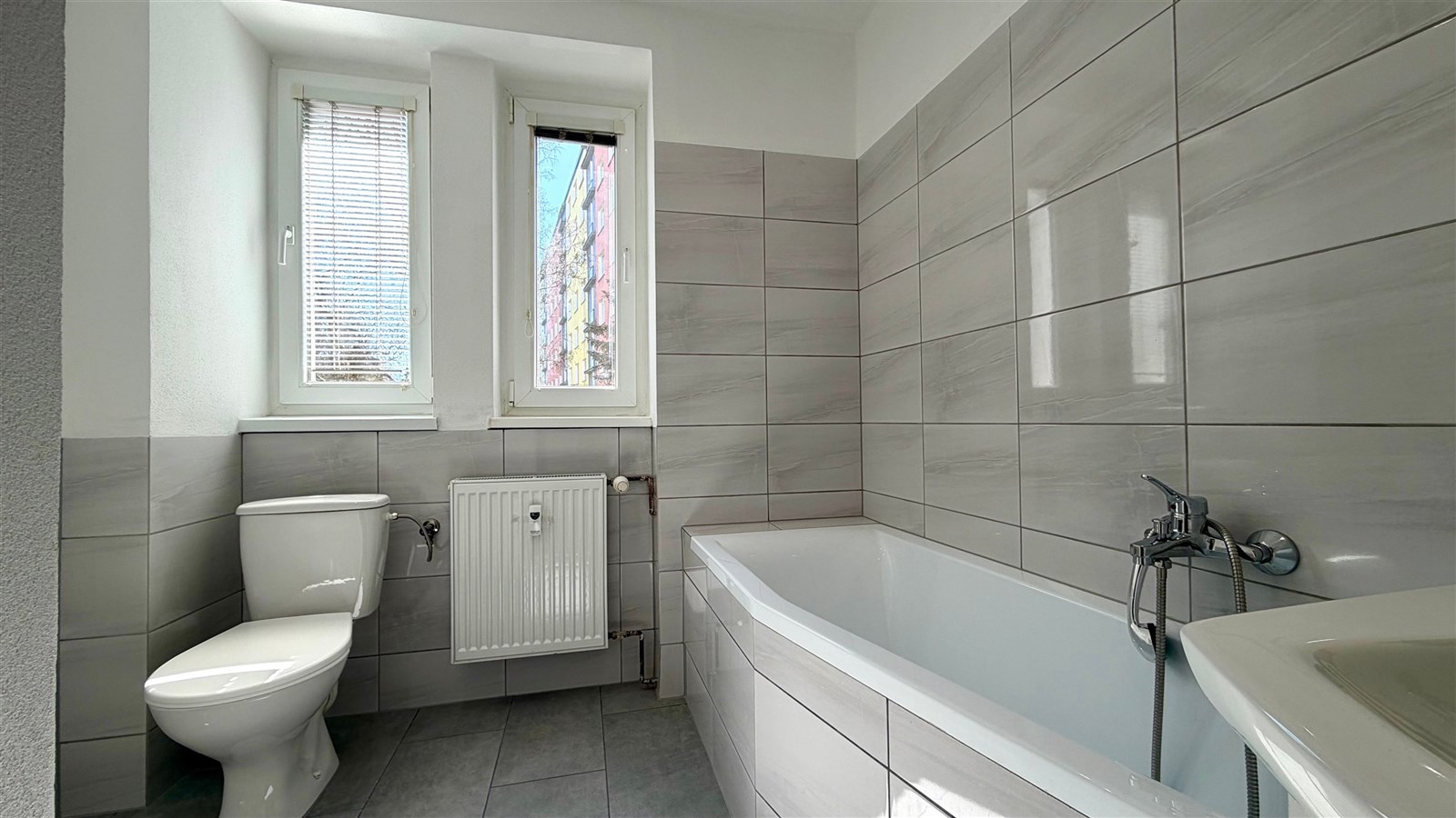 Koupelna s moderní dlažbou a obkladem, vanou a oknem pro denní světlo, ideální pro komfortní bydlení