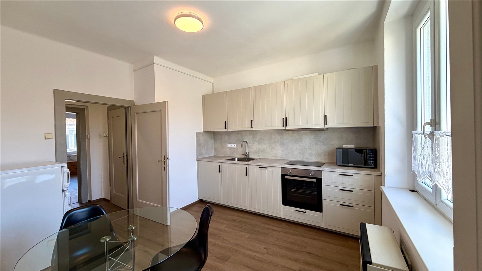 Moderní kuchyň s parketovou podlahou, světlá díky velkým oknům, vybavena vestavěnou troubou a mikrovlnnou troubou, ideální pro rodinné vaření