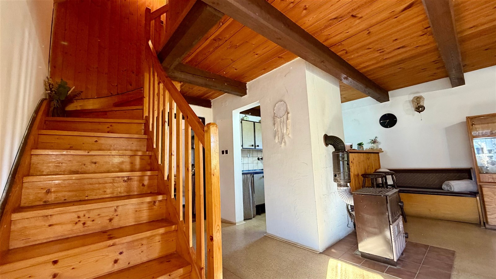 Rustikální schodiště s dřevěnými prvky, vedle rekreační místnosti s krbovými kamny a dřevěným obložením, vytváří útulnou atmosféru chalupy.