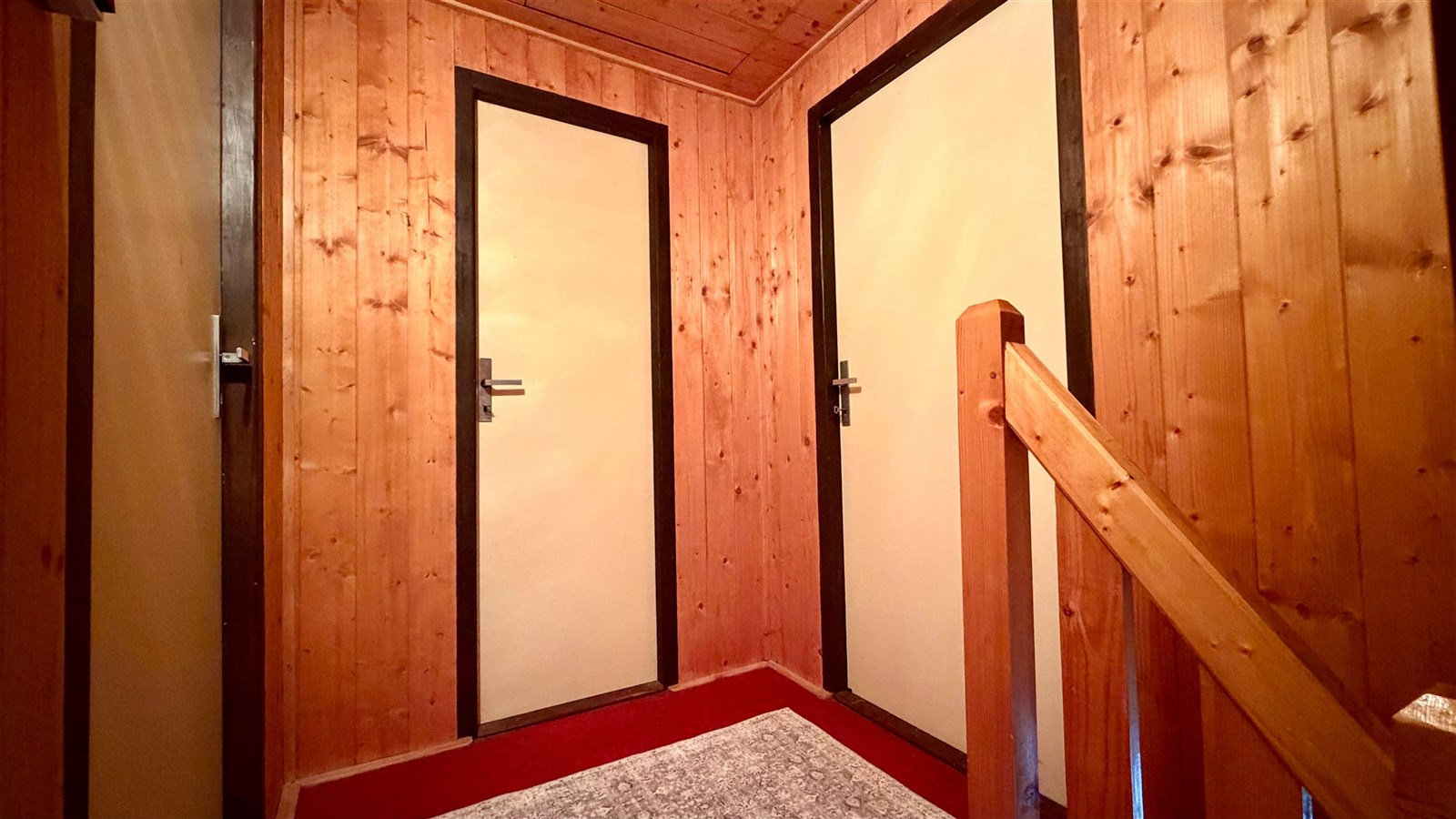 Chodba s dřevěným obložením, koberci a trojicí dveří, nabízí klasický styl. Teplé tóny a jednoduchý design vytvářejí útulnou atmosféru.